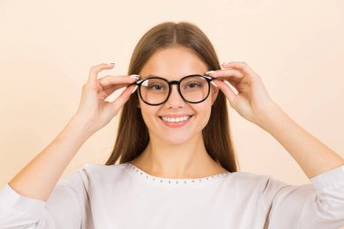 Bej arka planda gözlüklü güzel bir genç kadın.