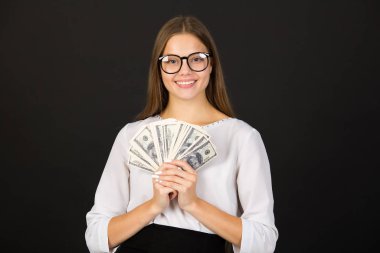 Siyah arka planda gözlüklü genç bir kadın, ellerinde dolarlarla.
