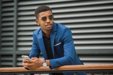 Mavi ceketli, elinde gözlüklü bir telefonla yakışıklı bir Afrikalı.