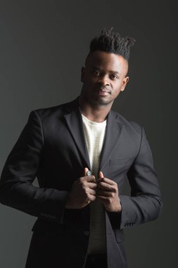 Gri arka planda siyah takım elbiseli yakışıklı Afrikalı adam.