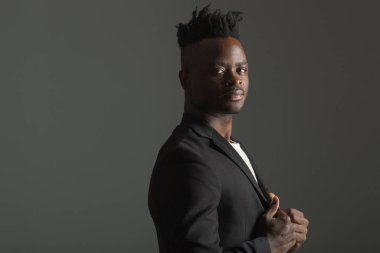 Gri arka planda siyah takım elbiseli yakışıklı Afrikalı adam.