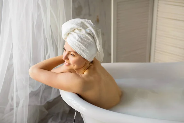 漂亮的年轻女子头戴毛巾躺在洗澡间里喝牛奶 — 图库照片