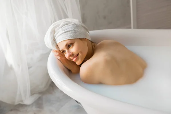 頭にタオルを被った美しい若い女性がミルク風呂に入っています — ストック写真