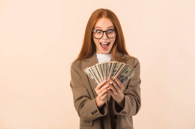 Bej arka planda ceketli, kırmızı saçlı güzel bir genç kadın. Elinde dolarlarla.