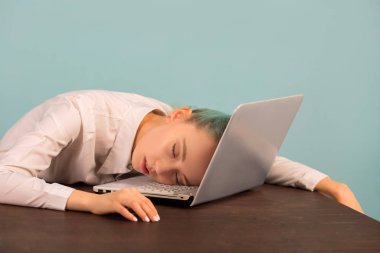 Güzel genç bir kadın dizüstü bilgisayarla masada uyuyor.