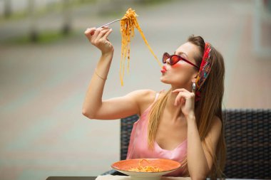 Güzel genç bir kadın bir kafede spagetti yiyor.