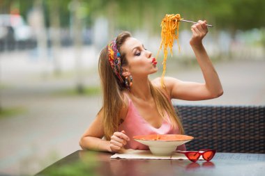 Güzel genç bir kadın bir kafede spagetti yiyor.