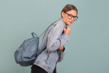 portrait of a beautiful young woman in glasses on a blue background with a backpack