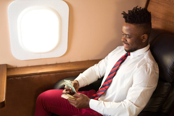 handsome african man in a white shirt in an airplane chair with dollars in his hands
