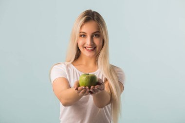 Ellerinde yeşil bir elma, mavi bir arka planı olan güzel genç bir kadın.