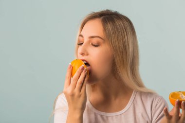 Ellerinde yeşil elma ve turuncu ellerle mavi arka planda güzel genç bir kadın.