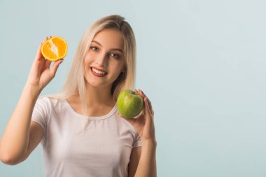Ellerinde yeşil elma ve turuncu ellerle mavi arka planda güzel genç bir kadın.