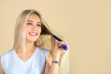 Güzel genç bir kadın bej bir arka planda saçını tarıyor.