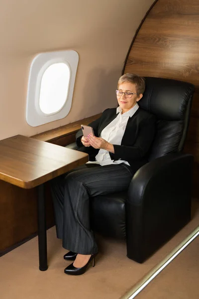 Piękna Starsza Kobieta Kabinie Prywatnego Samolotu Fotelu Telefonem Rękach — Zdjęcie stockowe