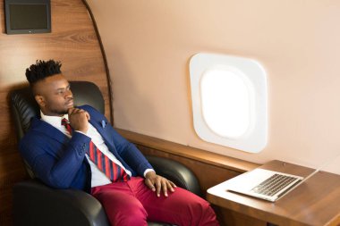Özel jet kabininde dizüstü bilgisayarlı, takım elbiseli yakışıklı Afrikalı genç adam.