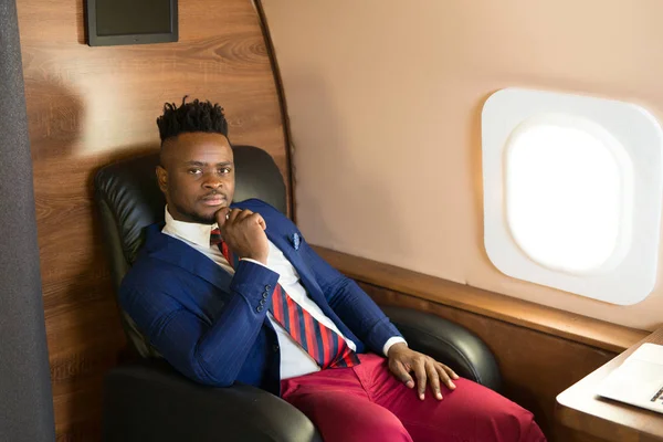 handsome african young man in suit in private jet cabin with laptop