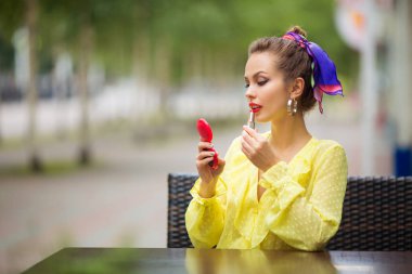 Güzel genç bir kadın rujla dudaklarını boyuyor.