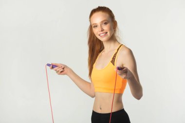 Beyaz arka planda kırmızı saçlı, ince, güzel bir kadın. Elinde ip atlayan biri var.