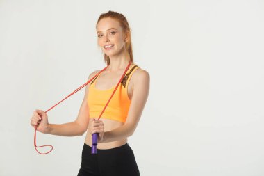 Beyaz arka planda kırmızı saçlı, ince, güzel bir kadın. Elinde ip atlayan biri var.