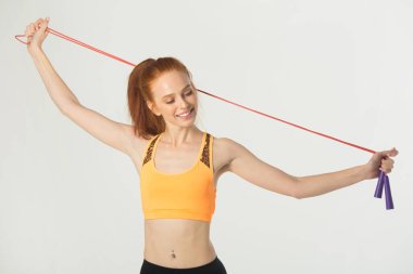 Beyaz arka planda kırmızı saçlı, ince, güzel bir kadın. Elinde ip atlayan biri var.