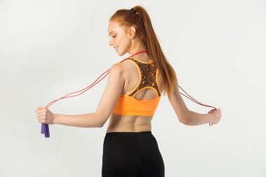 Beyaz arka planda kırmızı saçlı, ince, güzel bir kadın. Elinde ip atlayan biri var.