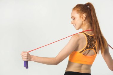 Beyaz arka planda kırmızı saçlı, ince, güzel bir kadın. Elinde ip atlayan biri var.