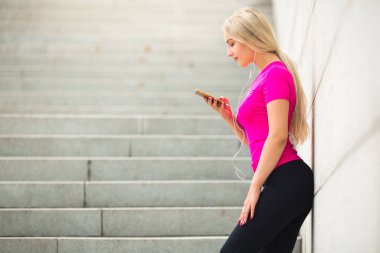 Yazın genç ve güzel bir kadın spor giyer. Kulaklıklarıyla sokakta. Elinde telefonuyla.