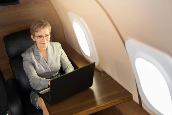 adult woman with short haircut in suit sits in private chair with laptop