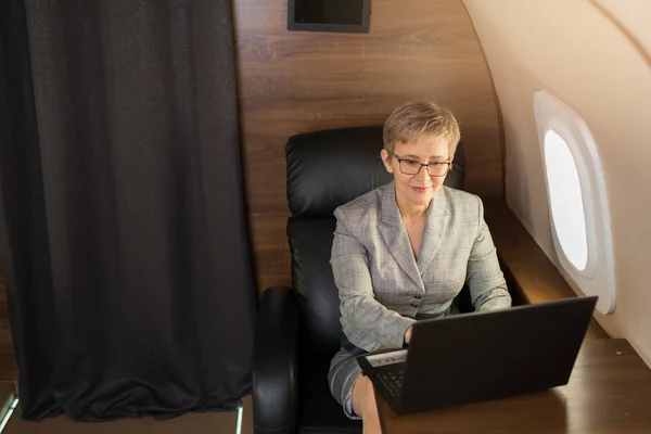 adult woman with short haircut in suit sits in private chair with laptop