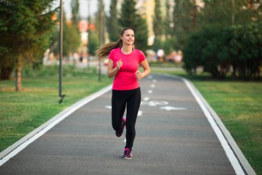 Güzel genç bir kadın yaz parkında koşu bandında koşuyor.