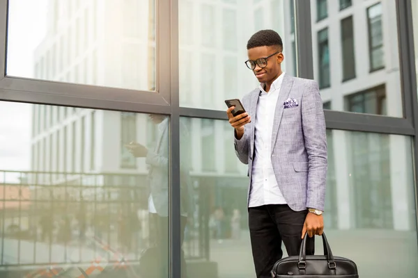 handsome young african man in a suit with a phone in his hands near a glass building