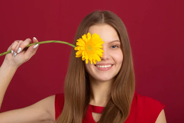 赤い背景に花を手にした美しい若い女性が — ストック写真