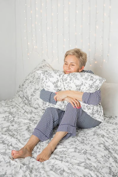 adult elderly woman in pajamas in bed in the bedroom with a pillow