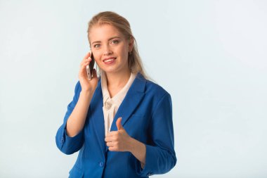 Mavi arka planda mavi ceketli, elinde telefon olan güzel bir kadın.