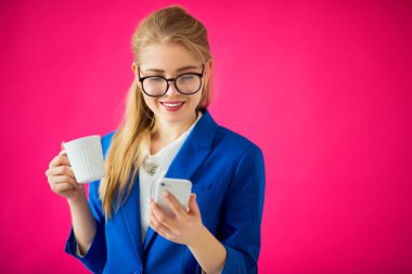 Pembe arka planda mavi ceketli, elinde telefon olan güzel bir kadın.