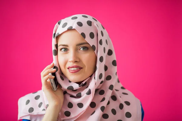 一个穿着围巾 粉色背景 手里拿着电话的漂亮年轻女人 — 图库照片