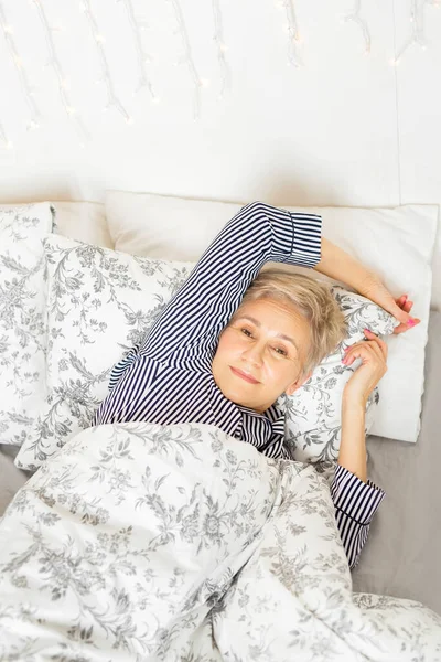 beautiful elderly woman in pajamas on the bed under the covers