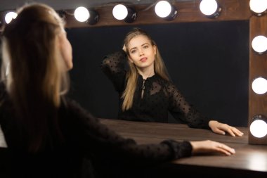 Güzel, genç bir kadın makyajlı ve saçı aynanın yansımasında.