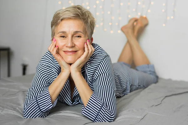 Yaşlanmış güzel, şık, yaşlı bir kadın yatakta yatıyor.
