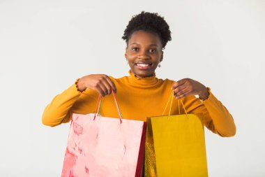 Beyaz arka planda, ellerinde paketleri olan güzel, genç bir Afrikalı kadın.