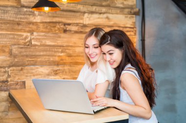 İki güzel genç bayan bir dizüstü bilgisayarla masada oturuyorlar.
