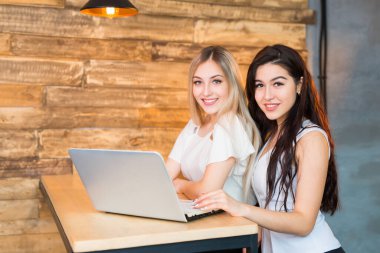 İki güzel genç bayan bir dizüstü bilgisayarla masada oturuyorlar.