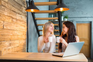 İki güzel genç bayan bir dizüstü bilgisayarla masada oturuyorlar.