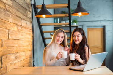 İki güzel genç bayan bir dizüstü bilgisayarla masada oturuyorlar.
