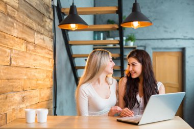İki güzel genç bayan bir dizüstü bilgisayarla masada oturuyorlar.