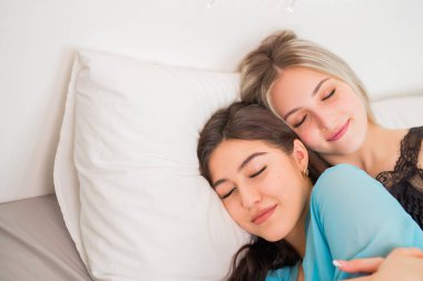 İki güzel genç kadın yatak odasında yatağın üstünde.