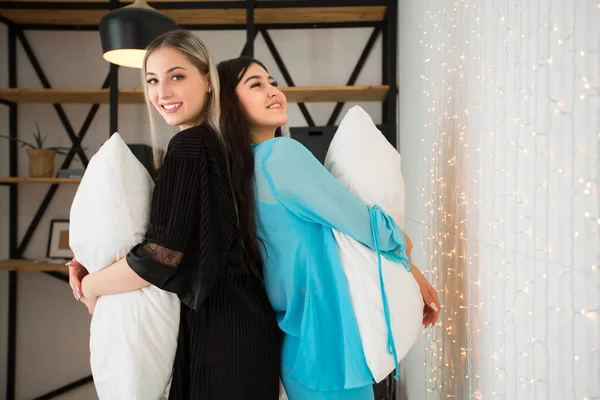 two beautiful young women on the bed play with pillows