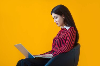 Sarı arka planda dizüstü bilgisayarı olan güzel genç bir kadın.