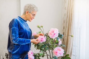 Ev çiçekleri yakınında şık bir yetişkin kadın.