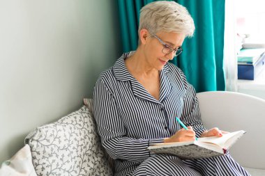 Yaşlı kadın pijamalarıyla yatakta oturuyor.